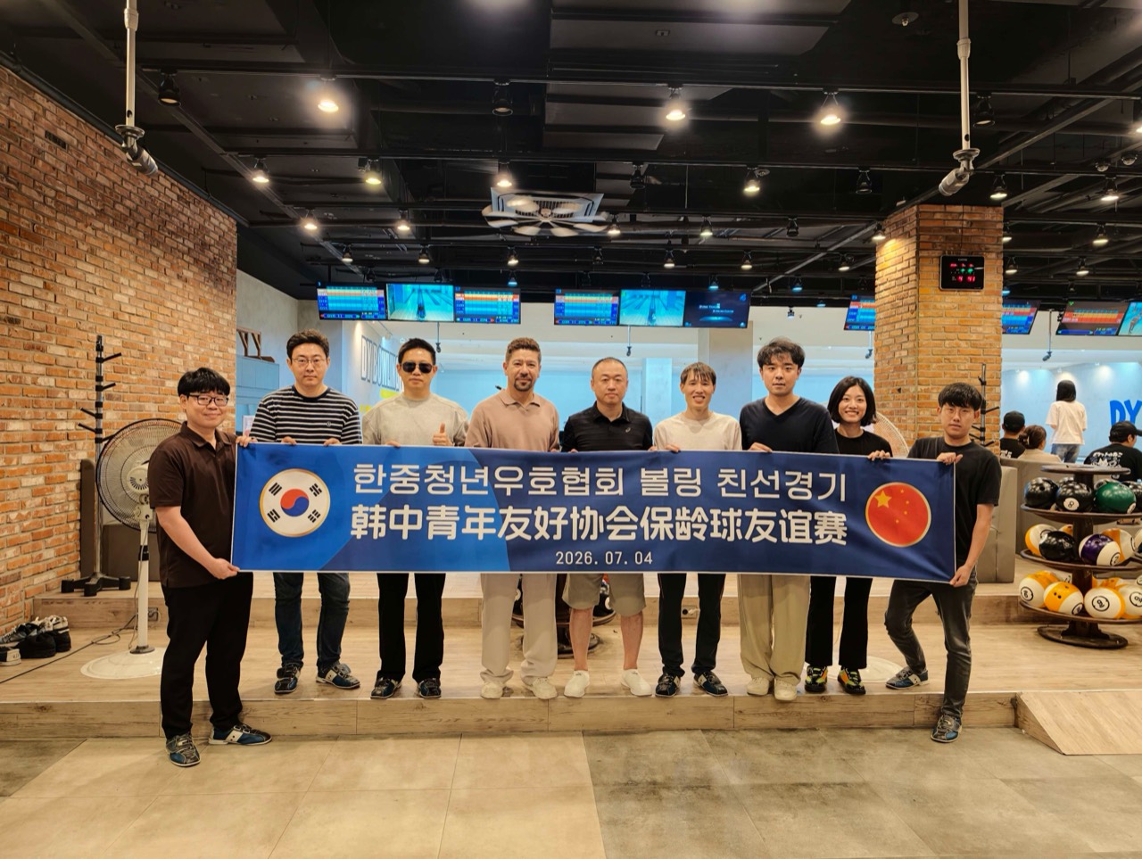 볼링장에서 한중청년우호협회 볼링 친선경기 현수막을 들고 기념 촬영하는 참가자들