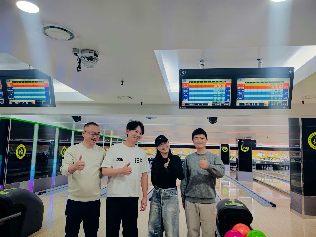 볼링장 레인 앞에서 엄지를 들어 보이며 함께 기념 촬영하는 네 사람