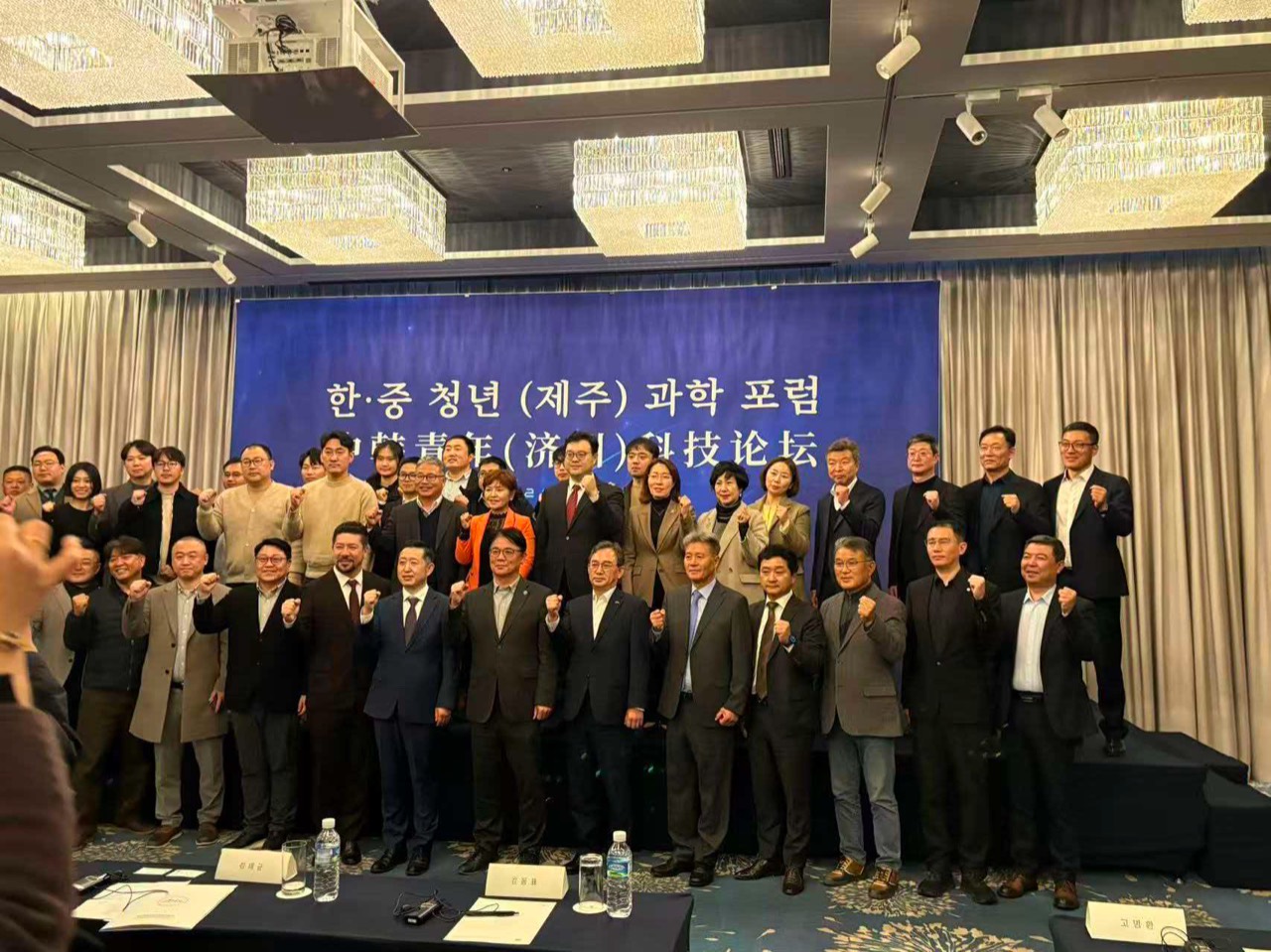 한·중 청년 제주 과학 포럼 현수막 앞에서 주먹을 들어 보이며 단체 기념 촬영하는 참가자들